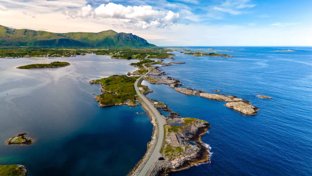 A breathtaking coastal road stretches along Norway's picturesque shore, surrounded by tranquil waters and lush greenery under a vibrant sky. Atlantic ocean road Norway