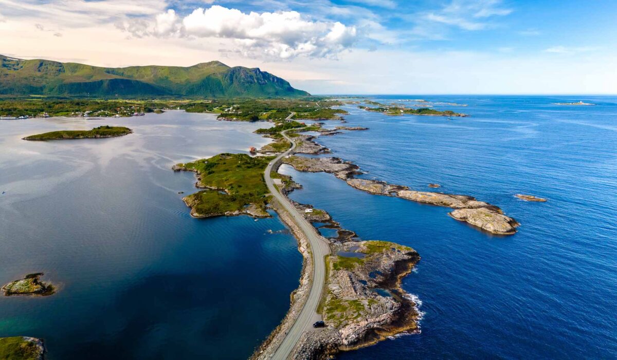A breathtaking coastal road stretches along Norway's picturesque shore, surrounded by tranquil waters and lush greenery under a vibrant sky. Atlantic ocean road Norway