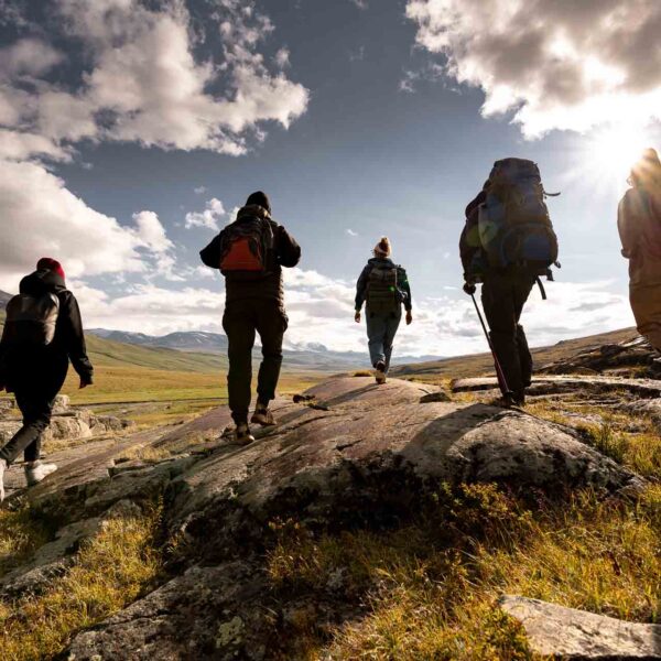 Group of tourist silhouettes with backpacks walks in sunset mountains